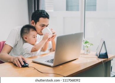 Working From Home Of Asian Little Son Helping Father Drinking Coffee Between Working With Laptop Computer Notebook At Workplace Happy Family Together At Home Concept.