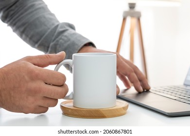 Working at home and drink coffee from 10 oz white ceramic mug. White cup copy space mockup for your design. Business concept with office desk and laptop