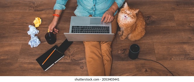 Working From Home With Laptop, Alexa Smart Voice Assistant, Cup Of Coffee And Ginger Pet Cat. Man Sitting On Laminate Warm Floor With Smart Phone. Remote Work.