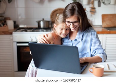 Working from home office with kid. Happy mother and daughter shopping online, using laptop together. Woman hugging child. Freelancer workplace at kitchen table. Female business, virtual communication.