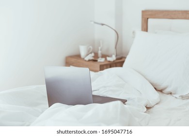 Working home quarantine self isolation lockdown concept. Laptop in unmade bed. Comfortable and cozy remote home office. Modern apartments with sunlight and minimalistic design. Stay safe in pandemic.