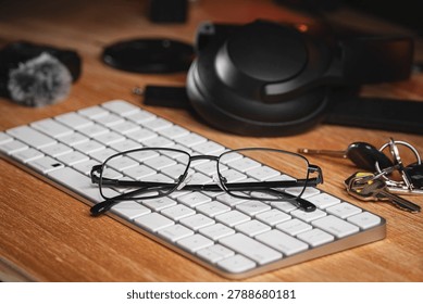 Working from home setup with spectacles resting on a white wireless keyboard, surrounded by headphones and car keys, representing a modern creative workspace