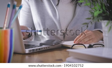 working at home, smart working. woman is set down and writes on notebook and tapping laptop and smartphon on desk. Girl uses more technological device for communicate and work.