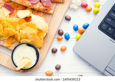 Working At Home And Snacks. Home Office With Unhealthy Lifestyle. Leisure With Laptop And Fast Food. Potato Chips, Pizza, Candies And Computer On The Table. Top View.