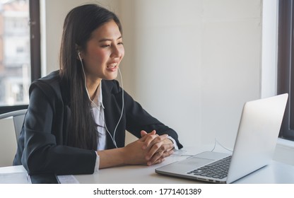 Working from home using internet communication concept. Asian young woman wear earphones talking  in video conference with business partners and worker team via online internet at her home.
