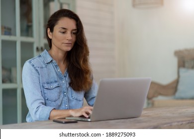 Working At Home Woman With Phone And Computer Sitting On The Table. Home Blurred Background.