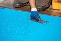 Working In Knee Pads, Mason Hand Spreading Soft Rubber Crumbs. Outdoor Soft Coating And Floor Covering For Sports. Rubber Mulch For Safety. Selective Focus. 

