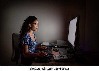 Working Late At Night On Computer. Asian Woman At Office Desk Staring At Desktop Screen Wearing Blue Light Eyewear Glasses To Protect From Eye Strain For Long Hours Of Work.