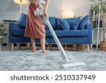 Working lifestyle concept Young Asian woman uses a cordless vacuum cleaner to clean the floor in the living room. Vacuum the floor, sofa, daily routine and housework.