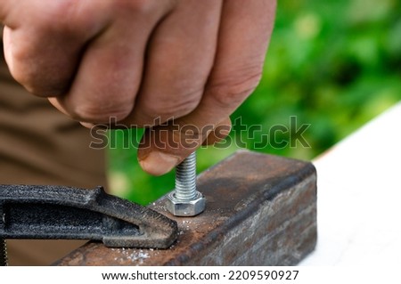 Working with metal. A man's hand screws a bolt into a metal nut
