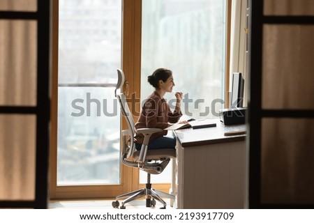 Working at modern home office. Young female architect interior designer sit at desk on ergonomic chair doing job project on desktop pc. Millennial indian woman study at domestic workplace