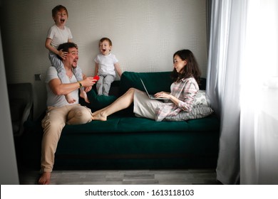 Working mom with a laptop and dad with a phone and children sons, authentic lifestyle in a real room. Concept parent freelancer, emotional kids.