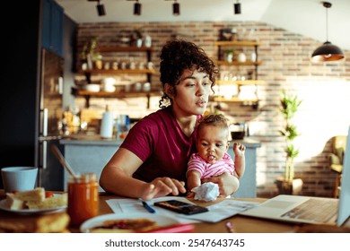 Working mom multitasking with baby while using laptop at home