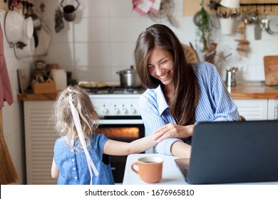 Working Mom Works From Home With Kid. Happy Mother And Daughter Have Fun. Successful Woman And Cute Child Using Laptop. Freelancer Workplace In Kitchen. Female Business. Lifestyle Authentic Moment