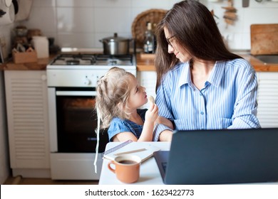 Working Mom Works From Home Office. Happy Mother And Daughter Look To Each Other. Woman And Cute Child Using Laptop. Freelancer Workplace In Cozy Kitchen. Female Business, Kindness, Care. Lifestyle.