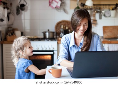 Working mom works from home office. Happy mother and daughter smiling. Successful woman and cute child using laptop. Freelancer workplace in cozy kitchen. Female business. Lifestyle authentic moment.