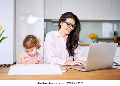 Working mother concept. Young woman working on laptop with her child from home