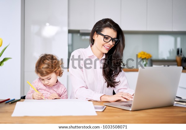 Working mother concept. Young woman working on\
laptop with her child from\
home