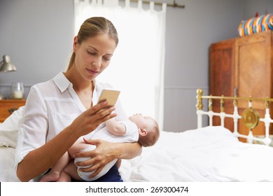 Working Mother Holding Baby And Checking Mobile Phone