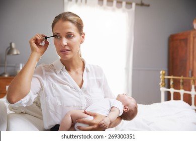 Working Mother Holding Baby And Putting On Make Up