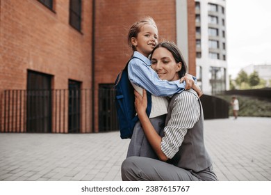 Working mother hugging daughter in front of the school building, and heading to work. Concept of work-life balance for women. - Powered by Shutterstock