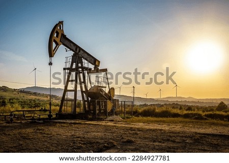 Working Oil pump and wind turbines at sunset. Industrial theme