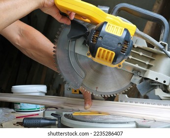 working on a circular saw in a workshop, male muscular hands lower the handle and blade of a miter saw to cut off the edge of a wooden fillet