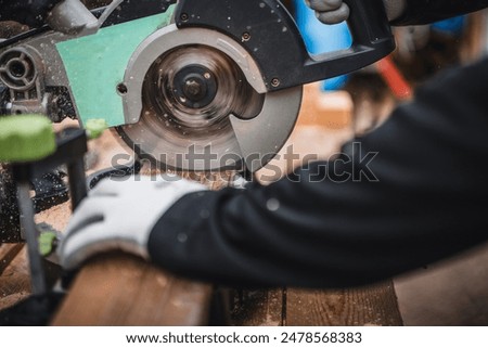 Working on a circular saw in a workshop. Male muscular hands lower the handle and blade of a miter saw to cut off the edge of a wooden fillet.