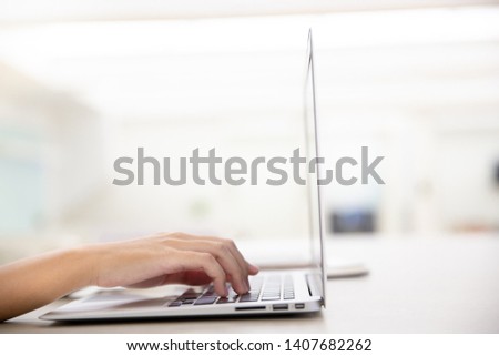 Working on new project with notebook computer flare light, blurred office building background. Close up of young female hands using laptop in modern office or loft near by the window.