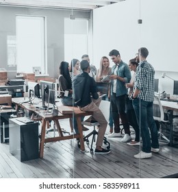 Working as one team. Full length of young modern people in smart casual wear having a meeting while standing behind the glass wall in the creative office - Shutterstock ID 583598911