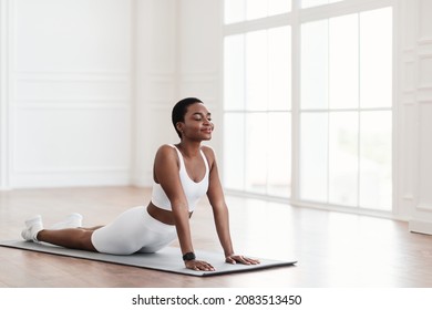 Working Out. Calm black woman stretching practicing yoga, doing Cobra exercise, lying in Bhujangasana pose or standing in upward-facing dog posture on fitness mat, breathing and meditating, copy space - Powered by Shutterstock