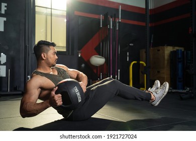 Working out at GYM concept. Young Asian handsome man working out his abdominal muscles by holding the medicine twist left and right sitting in the modern loft gym. Health and fitness concept.