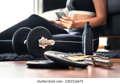 Working out at home with online fitness course, workout video or personal trainer service in phone. Health or sport mobile app in cellphone. Fit woman with smartphone and gym equipment.