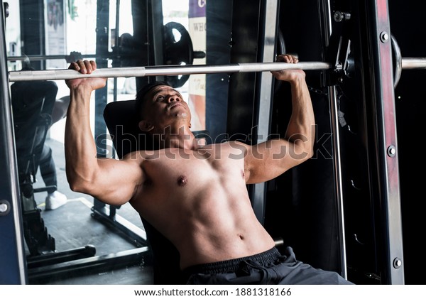 Working\
out and training scene - A shirtless asian 40 year old fit male\
does incline bench presses on a Smith\
Machine.