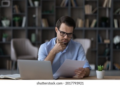 Working with papers. Serious millennial male entrepreneur work at home office alone hold read document hardcopy think on conditions terms. Focused young man engaged in paperwork edit text of agreement - Shutterstock ID 2017793921