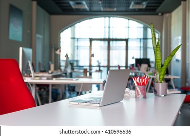 Arbeitsplatz auf grauem Tisch mit Laptop-grün blblblühenden Stuhl und Stifte im modernen Büroinnere mit großem Fenster auf Hintergrund