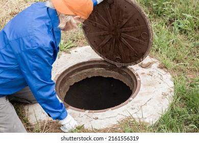 A working plumber opens a sewer hatch. Maintenance of septic tanks and water wells. - Shutterstock ID 2161556319