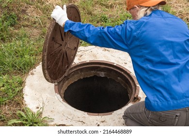 A working plumber opens a sewer hatch. Maintenance of septic tanks and water wells. selective focus - Shutterstock ID 2164468889