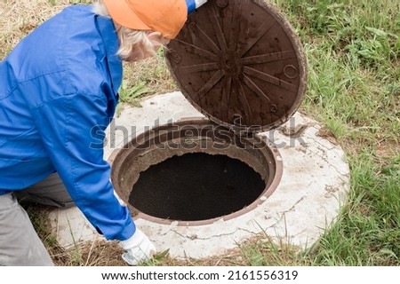 A working plumber opens a sewer hatch. Maintenance of septic tanks and water wells.
