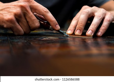 Working process of the leather belt in the leather workshop. Man holding crafting tool and working. He's making a slot line for decorating. Tanner in old tannery. Wooden table background - Powered by Shutterstock