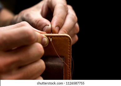 Working process of the leather belt in the leather workshop. Man holding crafting tool and working. He is sewing to make a walet. Tanner in old tannery. Wooden table background - Powered by Shutterstock