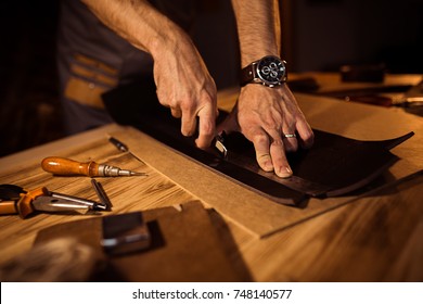 Working process of the leather belt in the leather workshop. Man holding crafting tool and working. Tanner in old tannery. Wooden table background. - Powered by Shutterstock