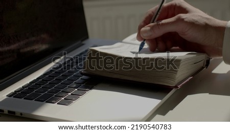 Working process. Recording thoughts and ideas in a notebook. Man hand in suit makes notes with pen in a paper diary at laptop, closeup. Skill of writing by hands, penmanship.