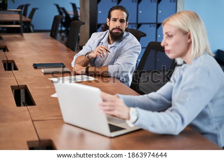 Working process. Serious bearded man peeping at the laptop screen while his female colleague explaining something to him. Work process concept