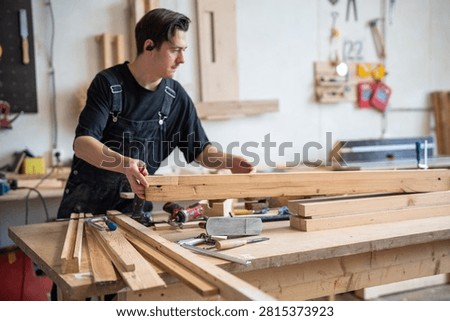 Working progress in carpentry workshop, concentrated man restorer choosing and selecting wooden planks, confident master woodworker placing details of window frame at worktable, restoration process.