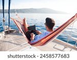 Working in sea traveling. Man with laptop in beach hammock. Summer vacation, living on yacht. Successful freelancer using computer. Workplace on nature outdoors, home office. Business lifestyle