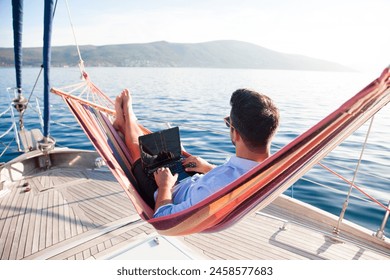 Working in sea traveling. Man with laptop in beach hammock. Summer vacation, living on yacht. Successful freelancer using computer. Workplace on nature outdoors, home office. Business lifestyle