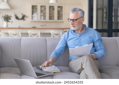 Working serious old senior elderly businessman paying domestic bills online using laptop, counting, paperwork, home office. Social distancing concept. Senior life. Freelance remote work - Powered by Shutterstock