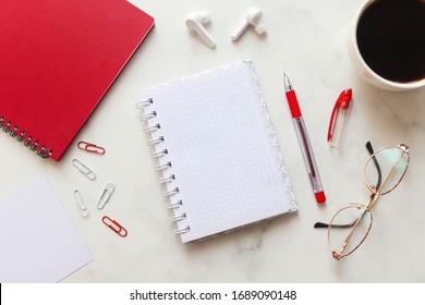 Working space with red notebook, women's glasses, cup of coffee and paper clips on marble background with copy space. Frame with notebook.Top view, flat lay.Office desk working space. Business concept