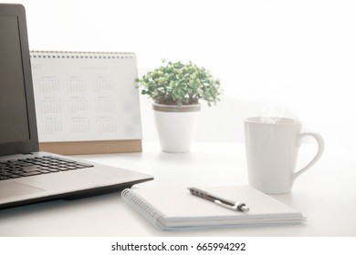 Working table consist of computer, calendar, notebook, pen, 
flowerpot Focus on the mug of coffee